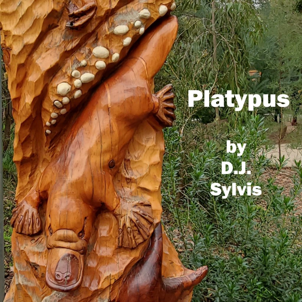 A carved wooden pillar showing a platypus, with tree branches and greenery in the background, with the legend, "Platypus, by D.J. Sylvis."